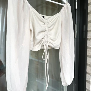 Bege Blus,topp - En bege blus i kortare modell. Som har snörning så man själv kan välja korthet på tröjan.  Tröjan är aldrig använd, så ny.  Färg: Bege Storlek: L