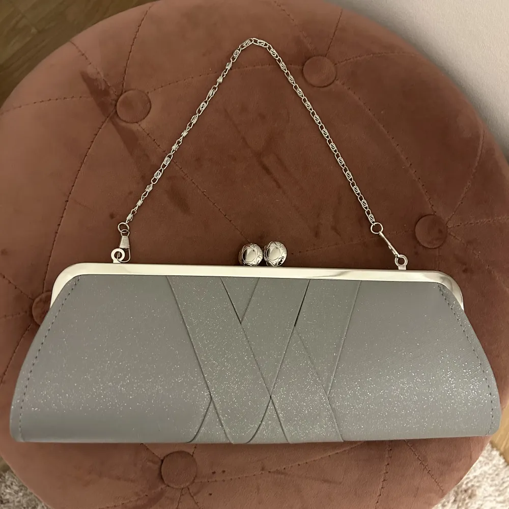 En grå glittrig clutch med silverdetaljer. Oanvänd. . Väskor.