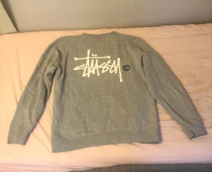 Stussy-tröja - En grå, långärmad tröja som jag inte är helt säker på är en äkta stussy tröja. Det finns 2 fläckar på framsidan som knappt syns, går inte bort. Trycket är sprucket och tröjan är nopprig,så den är i ganska använt skick. Skriv BARA vid intresse!!