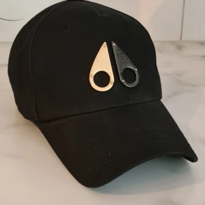 Moose knuckles keps - Svart Moose knuckles keps köpt på Johnells 2022 för 1299:-. Ett skrapmärke bak på spännet som knappt syns, tredje bilden.