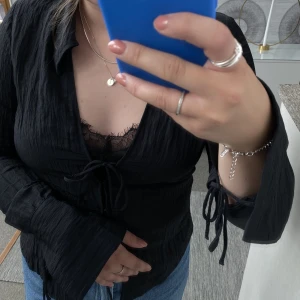 Svart knytblus - Svart knytblus från H&M. Fint skick. Det är två knytband framtill samt två knäppen. Ärmarna är långa och har slits där det även finns knytband. Önskas fler bilder är det bara att skriva