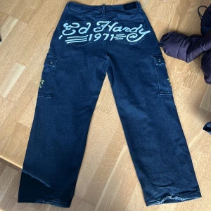 Ed Hardy cargo jeans  - Ett snyggt par ed Hardy jeans köpt för 1300 på Urban outfitters i Köpenhamn. Bra kondition förutom längst ner på benet där det har gått sönder pga att jag trampat på det. Hör av er för frågor!