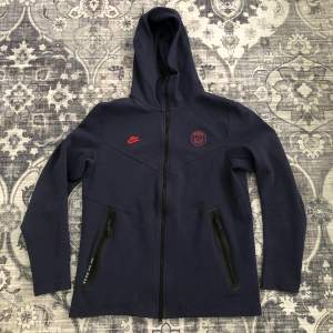 Nike x PSG hoodie/fleece i mörk blå färg med röda dekaler. (Går inte att få tag på längre/limited edition) Skick: Nyskick Köpt 2017/18 för 1200 ung och använts 2 gånger sen dess.  Säljer den för att den passar inte längre.