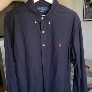 Ralph lauren skjorta  - Sparsamt använd! Mycket mörkblå färg som nästan ser svart ut, röd häst! Slim fit-modell.
