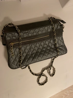 SILVER GRÅ VÄSKA FRÅN BOZZINI MED GULDFÄRGAD KEDJA - Jättefin väska från Bozzini. Köpt för ungefär 450kr. Väskan är i bra skick och har inga tydliga defekter eller synliga slitningar. Väldigt praktisk med många fack och flera dragkedjor. Kan mötas upp eller fraktas. Skriv för fler bilder eller för frågor.