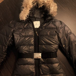 Moncler jacka dam  - Svart dunjacka med pälskrage och avtagbart skärp. Ok skick. Allt helt. Har extra monclerknappar som medföljer vb. 