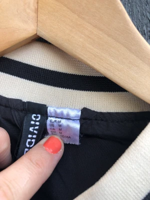 Snygg collegejacka från H&M!  - Cool oversize collegejacka från H&M!  Svart och beige med tryckknappar. Material: polyester. Storlek: M. Ingen anmärkning förutom lite smutsig på ena ärmmudden. 