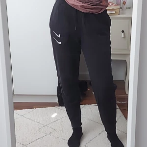 Svarta mjukisbyxor - Fina svarta mjukisbyxor med snöre i midjan! Fickor i sidorna och en på baksidan. Broderad swoosh logga på olika ställen och röd text tryck över fickan på baksidan. Väldigt sköna! Säljer då de har blivit lite för små för mig :)