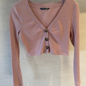 Tröja  - Långärmad rosa croppad tröja med knappar. Arm mått på 45cm och läng på 17 cm från armhålan samt midjemått på 33 cm. 