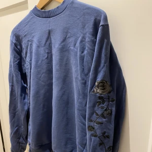 Collage tröja med blommor - Blå collage tröja med svarta/gråa blommor på utsidan av ärmarna. Från NA-KD. Passar mig som vanligtvis bär XS/S och är 170 