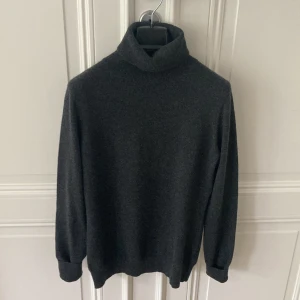 Polotröja i cashmere Uniqlo - Mörkgrå tröja i 100% cashmere från Uniqlo. Tröjan är knappt använd och i bra skick.