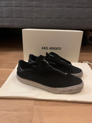 Axel arigato  - Säljer nu mina snygga Axel arigato skor i storlek 43. Men passar även 44. Skick 7/10. Box och påse ingår! OBS sömmen på ena skon har gått upp lite men går enkelt att fixa. Tveka inte att höra dig vid några funderingar! 