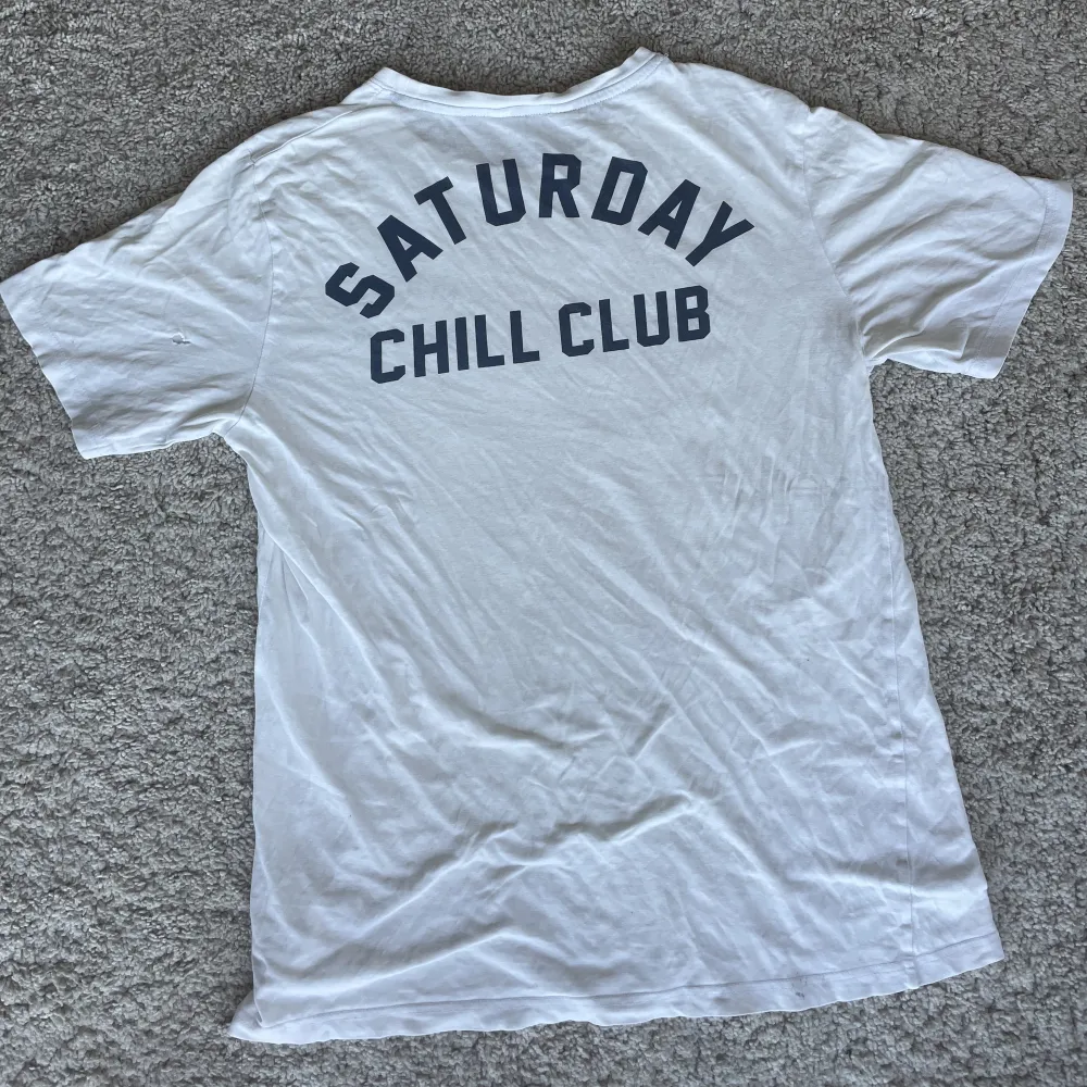 Skön, tunn och luftig t-shirt från H&M med trycket Saturday Chill Club över hjärtat och på ryggen. Skicket är ok. Har kommit små vita färgfläckar här och där men inget man ser eller tänker på. På vänster arm bak finns det ett ytterst litet hål, därav pris. T-shirts.