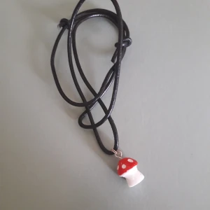 Svamp halsband - Handgjort halsband med svampsmycke på. Bandet är av svart läderräm, kan göras längre och kortare, som längst 60 cm.