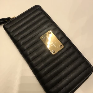 Plånbok  - Svart plånbok som inte är använd dock finns de små repor på metallskylten som syns på bilden men inget man ser om man inte tittar noga. 