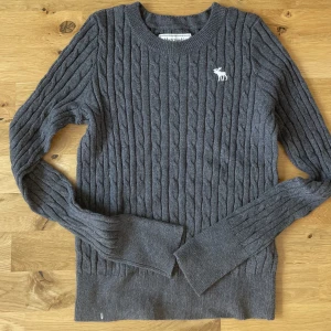Stickad tröja - Grå stickad abercrombie and fitch tröja. Aldrig använd (längst nere på tröjan råkade det sitta en vit fjäder när bilden togs)