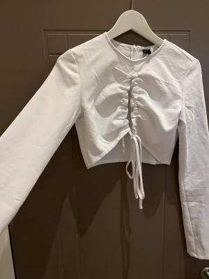 Topp - Vit topp från HM, öppen urringning där fram som man kan knyta hur man vill, ärmarna är i slits. Aldrig använd.