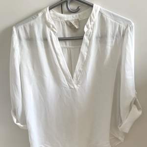 White blouse with V neck. The sleeves can be rolled up and tied with a golden button detail on the side of the sleeve. Size S, it looks wrinkled from being folded but can be ironed and it is back to top shape! Very cute with wide jeans and a jacket