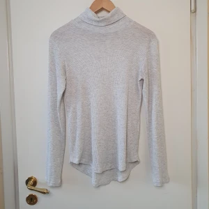Polotröja - Tunn ljusgrå polotröja med avrundat slut och något längre baktill.