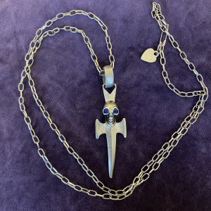 Halsband döskalle  - En halskedja med grinande döskalle med blåa stenar till ögon  Kedjan är ca 78 cm lång   Okänt material 