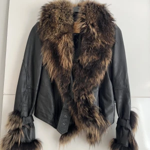 Skinnjacka med päls - Läderjacka i päls. Unik då detta är den enda som finns. Den köptes på en modevisning för några år sen & har endast använts ett par gånger sen dess. I fint skick, saknas en liten metallring runt ett av hålen i bältet (syns knappt). Äkta läder & päls
