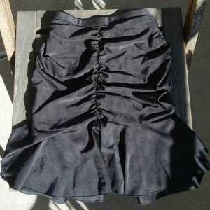 Svart kjol med scrunch och volang - Oanvänd kjol från cider. Tunt glansigt material men inte genomskinlig. Scrunch på rumpan och volang under rumpan. Får fina former i den