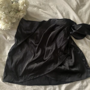 Svart omlott kjol satin - Svart omlottkjol i satinmaterial. Supersnygg o sexig perfekt för utekvällar! Aldrig använd. Storlek L men passar M-L 60kr