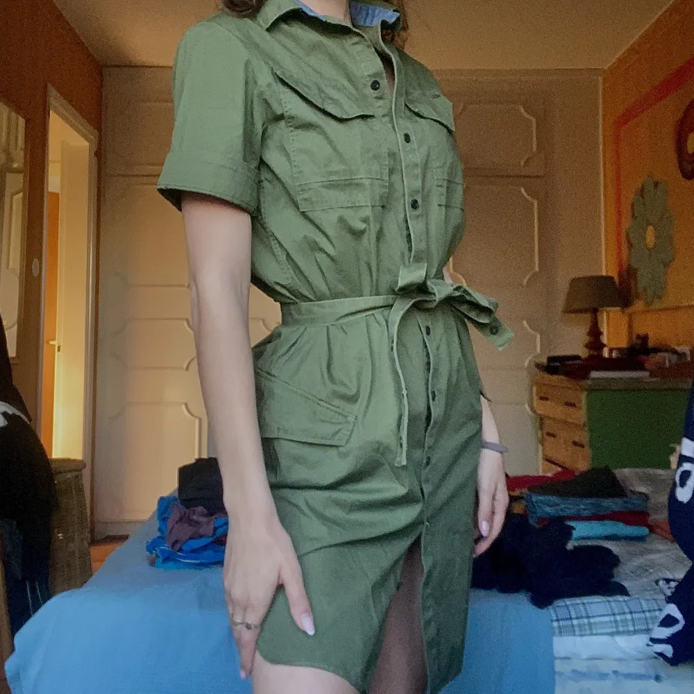 En klänning i cargostil.  Jag är 168 cm lång. Klänningen slutar straxt över knät Militärgrön Orginalpris 900. Klänningar.