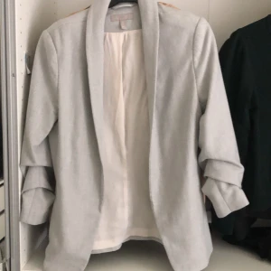 Kavaj - En jättefint kavaj i ljusgrå. Använt få tal gånger. Den har uppvikta ärmar som detaljer. Inga skador och är i nyskick i utseende. Vid intresse kan närmare bilder skickas. 