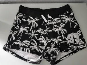 Svartvita mjukisshorts - Sköna mjukisshorts med snörning som är svarta med vita palmer på. Fint skick! 35% bomull och 65% polyester.