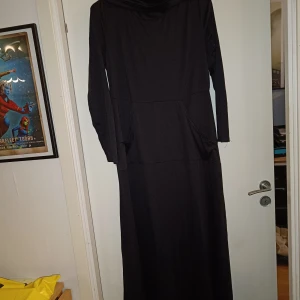 Lång svart klänning  - Lång svart klänning med ficka på magen och stor vikbar krage. Se bild för mått