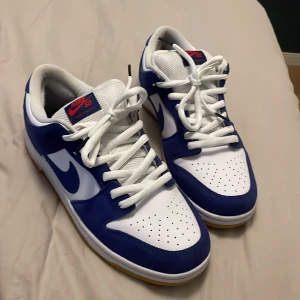 Nike SB Dunks LA Dodgers  - Säljer mina SB Dunks i grymt skick. Använda några gånger men inga större flaws finns. 9/10 skick.   Storlek: 43 (EU)  3 par skosnören följer med, vita,röda och blåa.   