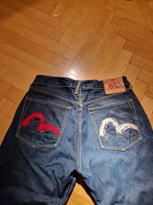 Evisu - 90-tal Evisu-jeans no.2 med seagull-tryck i rött och vitt. Lite baggy med lite smalare vid foten så att byxorna lägger sig på skorna. Väldigt bra skick, bara lite nött längst ner på ena benet. Storlek 32. 