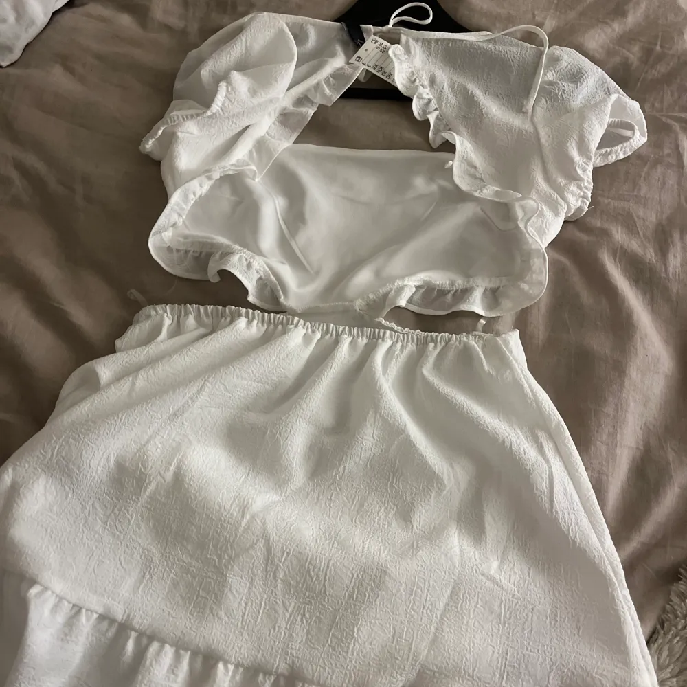 Hej jag säljer en vit klänning som är oanvänd och lappen finns kvar på klänningen, den är öppen i ryggen och vid sidorna av magen men de finns genomskinliga snören som håller upp den.. Klänningar.
