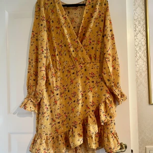 Gul/orange blommig sommarklänning - Söt blommig sommarklänning från BIKBOK, storlek L. Kan även passa M om man vill att klänningen ska sitta mer rakt och något lösare. Klänningen stängs med en dragkedja vid midjan.  Aldrig använd, inga märken eller spår av användning. 