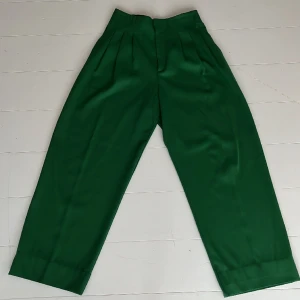 Vid kostymbyxa i ylleblandning - Gröna coola dressade byxor med vid passform och hög midja. Fickor fram och bak. Fint skick, som nya. Fin kvalitet som faller fint. Innerbenslängd 71 cm men går att utöka drygt 9 cm genom att ta ner fållen. 