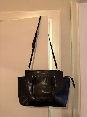 Skinnväska Coccinelle - Superfin svart skinnväska från italienska Coccinelle. Perfekt jobbväska med plats för laptop!  Tre innerfack och avtagbar axelrem.   H 29 cm B 33 cm  D 11 cm 