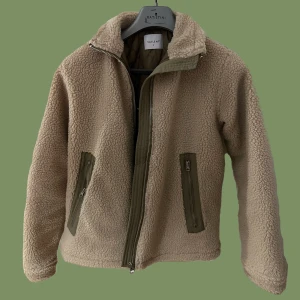 Teddy jacka från Carlings - Beige med gröna detaljer. Finns innerficka och ytterfickor. Sparsamt använd, jättemysig! 