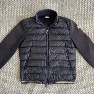 Moncler Cardigan - Säljer nu min fräscha mörkblåa Moncler cardigan. Jackan är i bra skick 7/10, lite solblekt samt ett litet hål på ärmen (bild 3). Storlek M sitter som en S/M. Självklart autentisk. Hör gärna av dig vid frågor eller fler bilder👊🏽😁