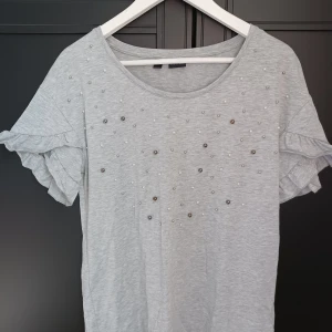 Tröja med pärlor  - En grå tröja med pärlor och volanger på ärmarna. Fint skick o skönt material.