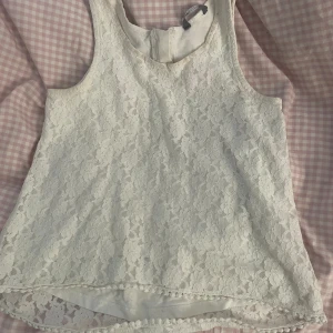 Vit topp - Vit topp med blommigt mönster, toppen är använd men är i princip i nytt skick. Den har dubbelt lager med en dragkedja på ryggen. 
