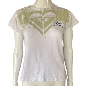 Roxy T-Shirt  - En y2k T-shirt i okej skick från Roxy. Storlek 10. Skulle säga skicket är 6/10. Nytvättad men maskinen är såpass dålig att den inte tar bort fläcken. Syns på bild fyra.  MÅTT: Axel till axel 35cm, ärmlängd 12cm, armhåla till armhåla 46cm & längd 55cm