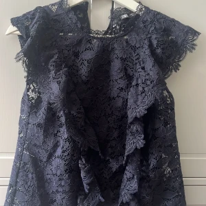 Mörkblå spetsblus - En elegant mörkblå spetsblus med volangdetaljer. Blusen har korta ärmar och en rund halsringning. Perfekt för festliga tillfällen. Inga tecken på användning❤️