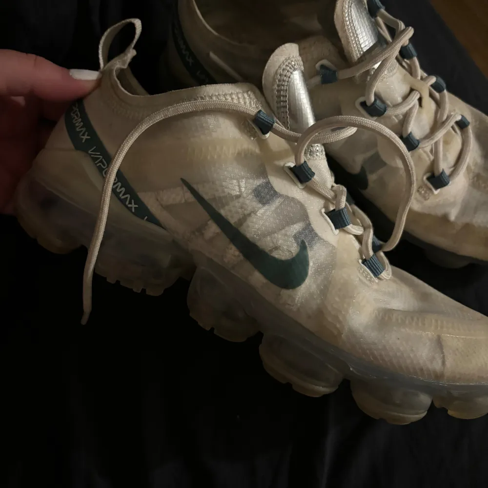 Ett par vita Nike Air Vapormax sneakers med blå detaljer och snörning. Skorna har en genomskinlig sula och är i välanvänt skick. sulan finns inte i skorna heller. Skor.