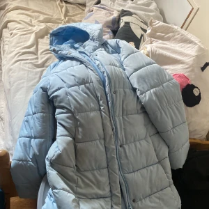 Blå lång vinterjacka  - En super fin ljus blå jacka ,lite längre stolek 160 luva finns på och den e super härlig att ha på sig när de är lite kallare