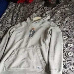 En grå hoodie från Jack & Jones med ett tryck av en hund klädd i jeansjacka och jeans på framsidan. Hoodien har en känguruficka och ribbstickade muddar vid ärmslut och nederkant.