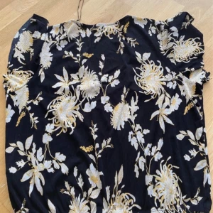 Svart blommig topp från Gina Tricot - En svart topp från Gina Tricot med ett blommigt mönster i vitt och gult. Toppen har korta ärmar och en v-ringad hals.