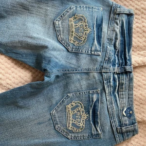 Jättesnygga lågmidjade jeans! - Snygga och trendiga lågmidjade jeans med kronor på bakfickorna! Inga skavanker förutom att några stenar har ramlat av. Bredd ca 38 cm, längd ca 95 cm, innerbenslängd ca 75 cm. Skriv i DM vid frågor 💗