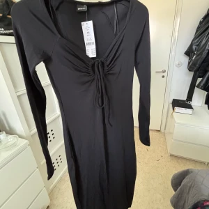 Svart klänning från Gina Tricot - En Oanvänd elegant svart långklänning från Gina Tricot med långärmad design. Klänningen har en knytning framtill och en v-ringad hals. 💕