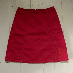 Röd Kjol - Röd kjol med orangea broderier. Storlek 38 men skulle säga att den passar M-L beroende på hur en vill att den ska sitta. Så fin och i bra skick men säljer för att den tyvärr inte kommer till användning. Hör av dig om du har några frågor! 